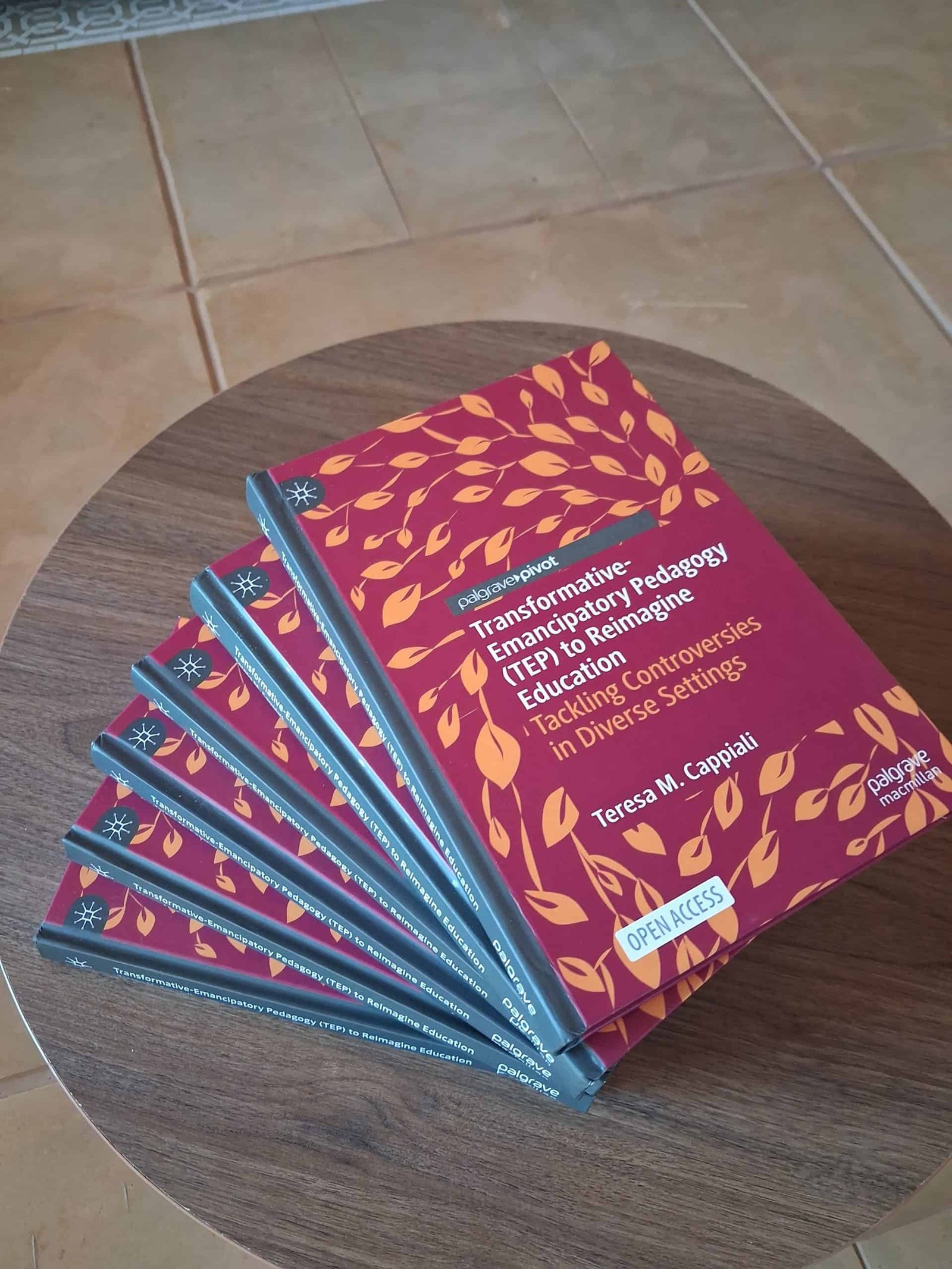 tep-book-copies-palgrave-macmillan-teresa-cappiali Multiple copies of the open access book Transformative-Emancipatory Pedagogy (TEP) to Reimagine Education by Teresa M. Cappiali, published by Palgrave Macmillan, fanned out on a wooden table.