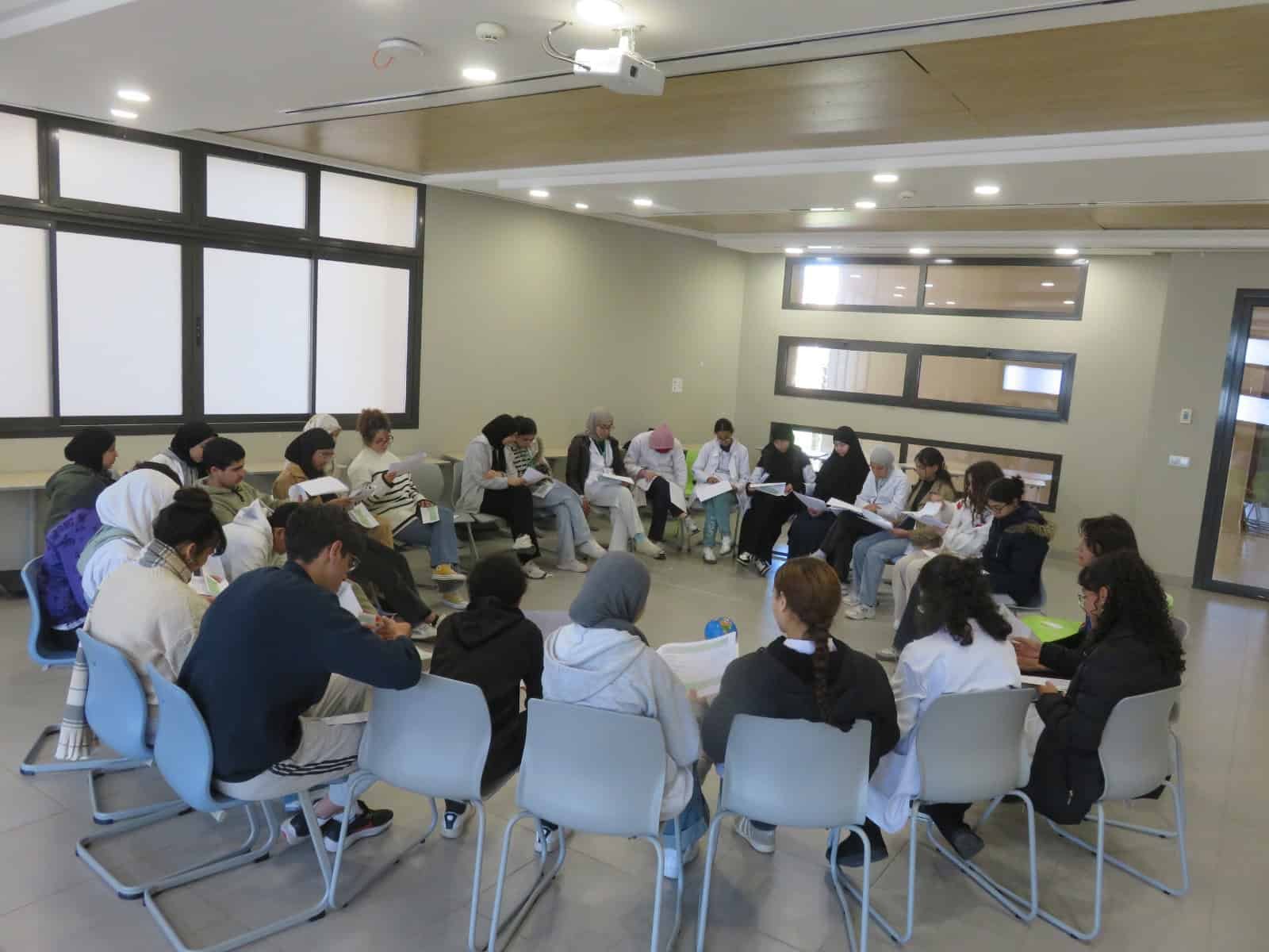 tep-full-circle-reading-activity-lycee-morocco-2026 All 30 students seated in a full circle during a reading and reflection activity in a Transformative-Emancipatory Pedagogy (TEP) session at Lycée Mohammed VI d'Excellence, Morocco, March 2026, with a globe visible at the centre of the circle.