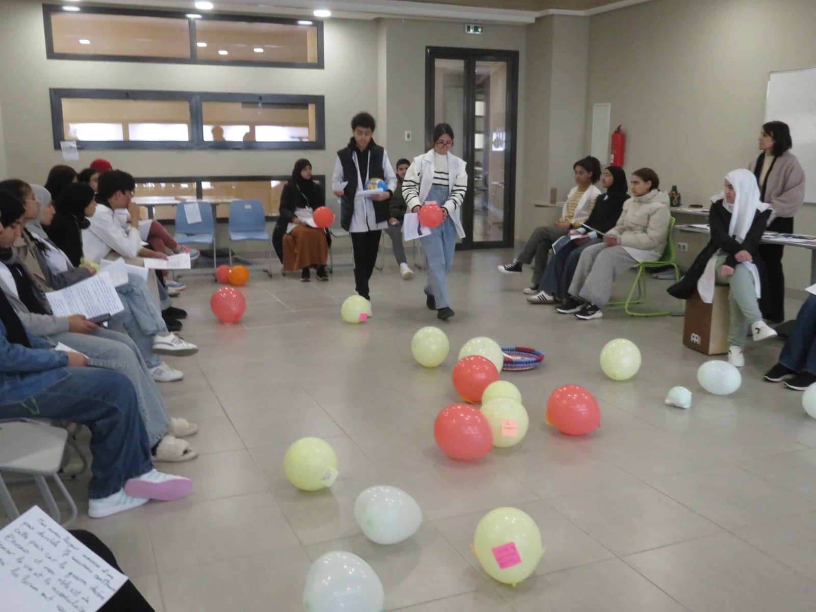 tep-workshop-balloon-simulation-activity-morocco Students seated in a circle watching two participants navigate colored balloons on the floor during an experiential learning simulation in a Transformative-Emancipatory Pedagogy (TEP) workshop in Morocco.