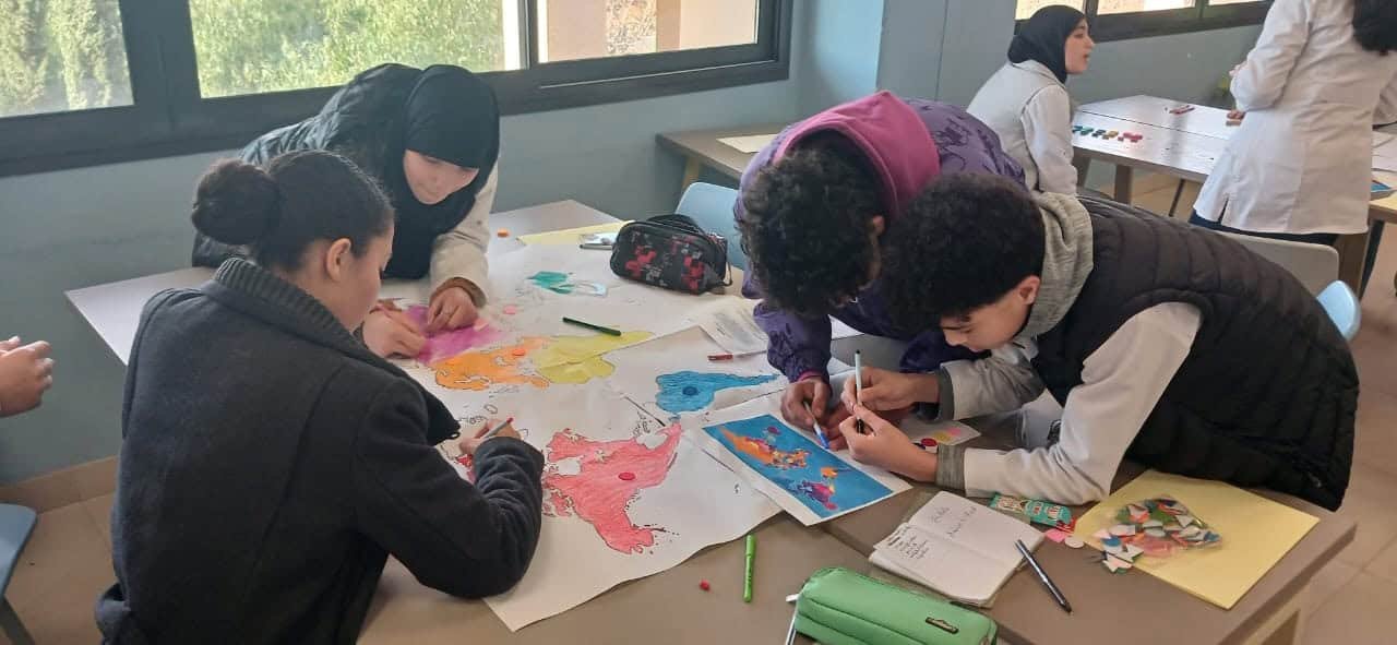 tep-workshop-collective-mapping-students-morocco Students collaboratively drawing and coloring a large world map on paper during a collective mapping activity in a Transformative-Emancipatory Pedagogy (TEP) workshop in Morocco, February 2026.