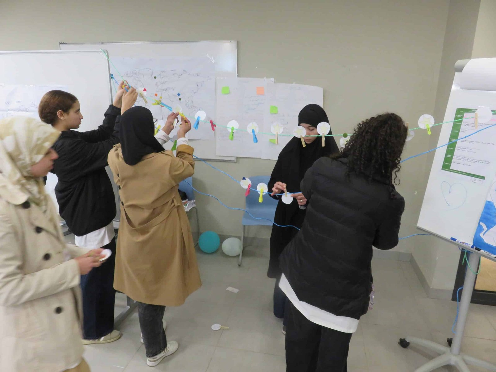 tep-workshop-pedagogy-of-hope-creative-activity-morocco Students collaboratively assembling a creative string installation with paper circles and colorful pegs during a pedagogy of hope activity in a Transformative-Emancipatory Pedagogy (TEP) workshop in Morocco, with maps and notes visible on the wall behind them.