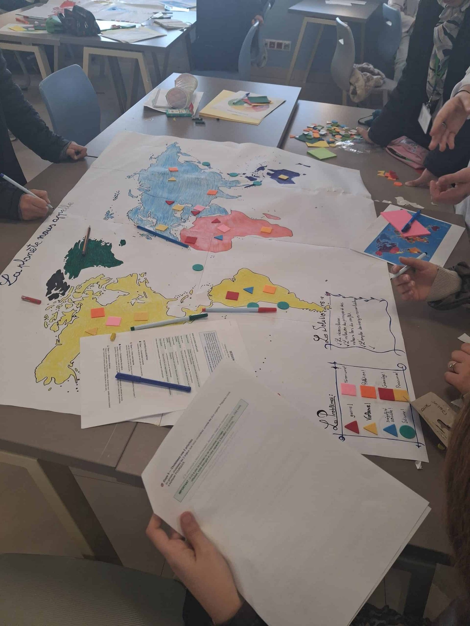 tep-collective-mapping-students-world-map-problems-solutions-morocco-feb-2026 Students collaboratively building a colored world map titled "La planète nous appelle" (The planet is calling us), identifying global problems (war, violence, social inequality, earthquakes) and proposing solutions including renewable energies and inclusive values, during a Transformative- Emancipatory Pedagogy (TEP) collective mapping activity, Lycée Mohammed VI d'Excellence, Morocco, February 2026.
